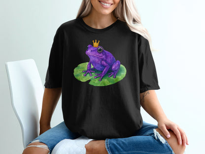 Purple frog with crown sits on a lily pad on a black t-shirt.