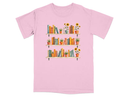 Pink t-shirt with a watercolor illustration of three bookshelves filled with books and potted plants.