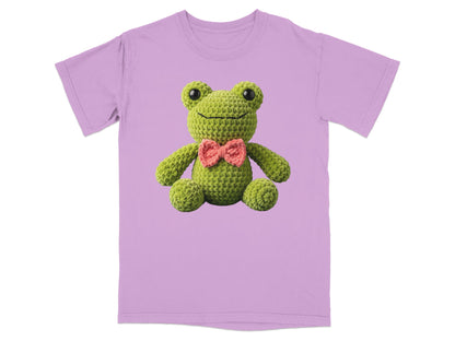 Crocheted green frog with pink bowtie on a lavender t-shirt.