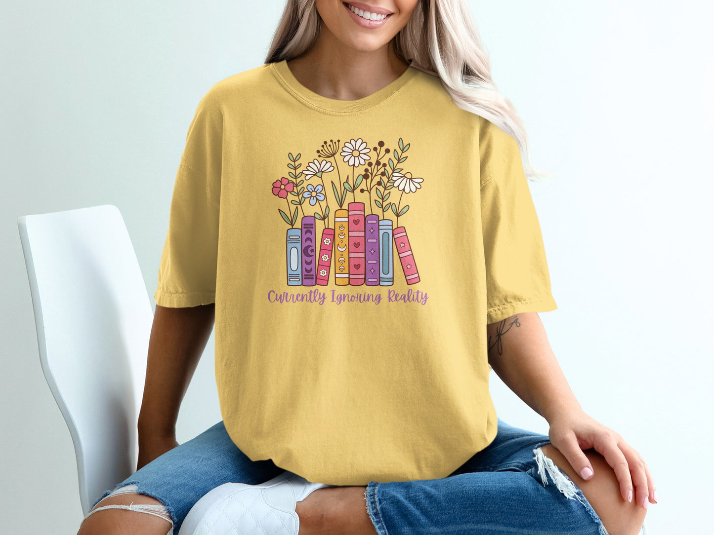 Yellow t-shirt with books and flowers, reads "Currently Ignoring Reality".