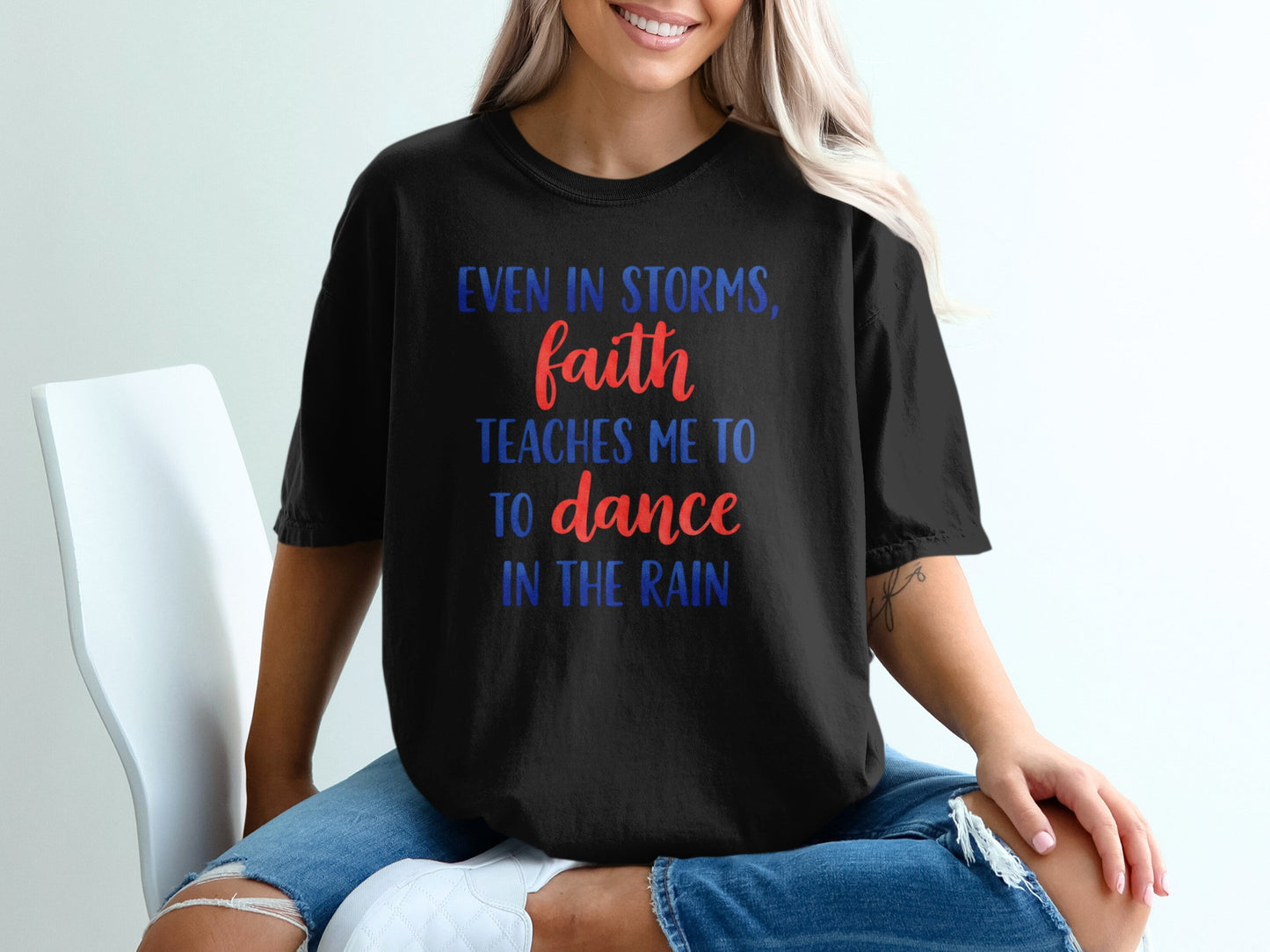 Black t-shirt with red and blue text: "Even in storms, faith teaches me to dance in the rain."