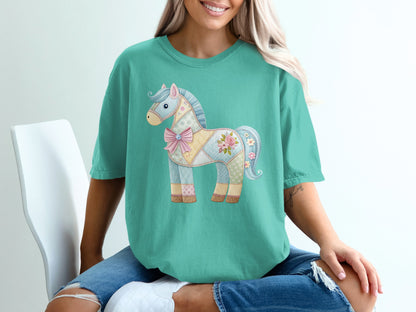Teal t-shirt with a pastel patchwork unicorn design featuring floral accents and a pink bow.