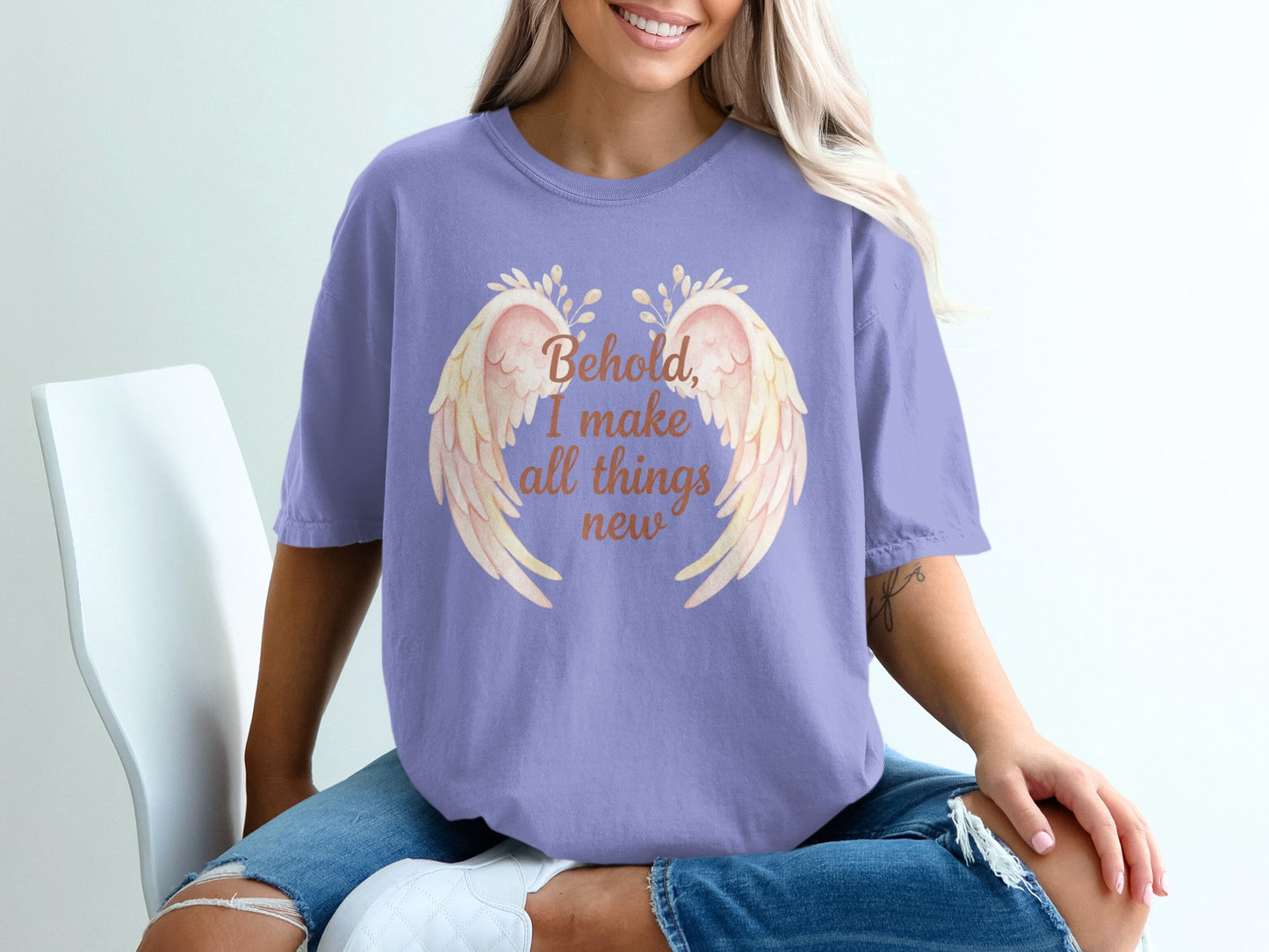 Purple t-shirt with "Behold, I make all things new" text and angel wings.