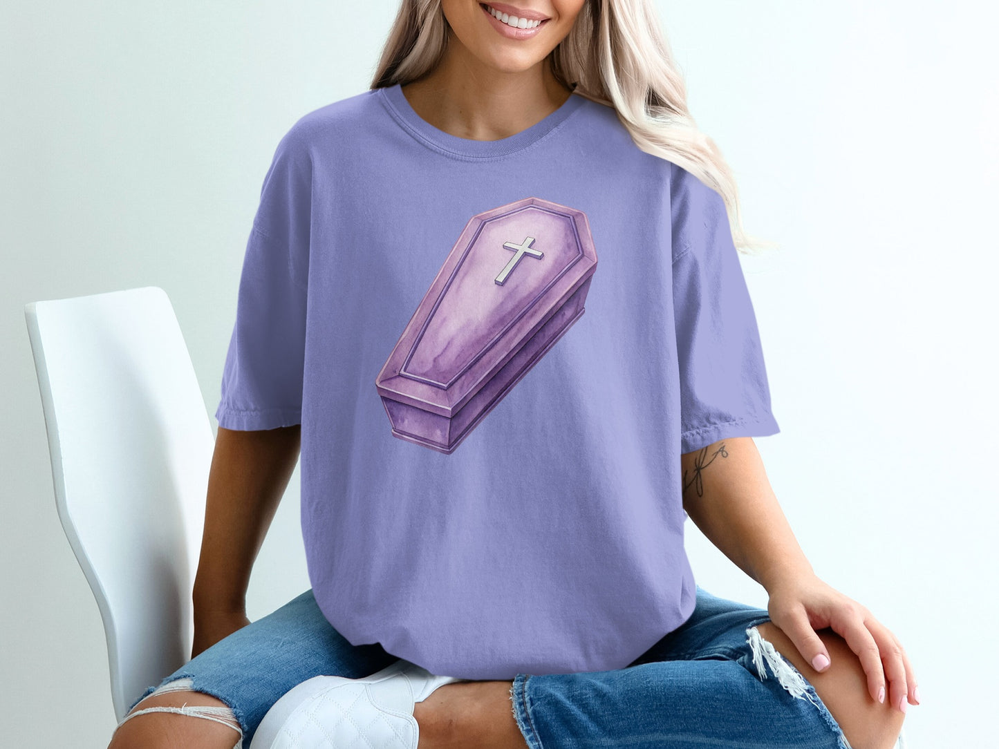 Purple t-shirt featuring a watercolor illustration of a coffin with a cross.