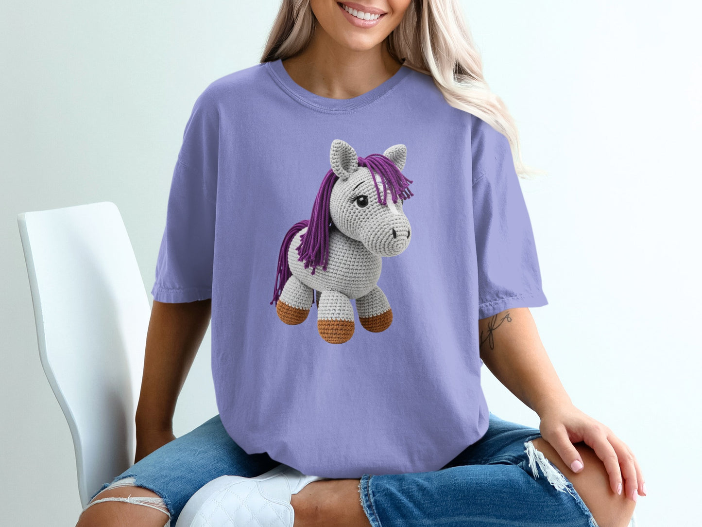 Crocheted gray horse with purple mane and tail on a purple t-shirt.