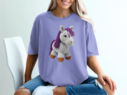Crocheted gray horse with purple mane and tail on a purple t-shirt.