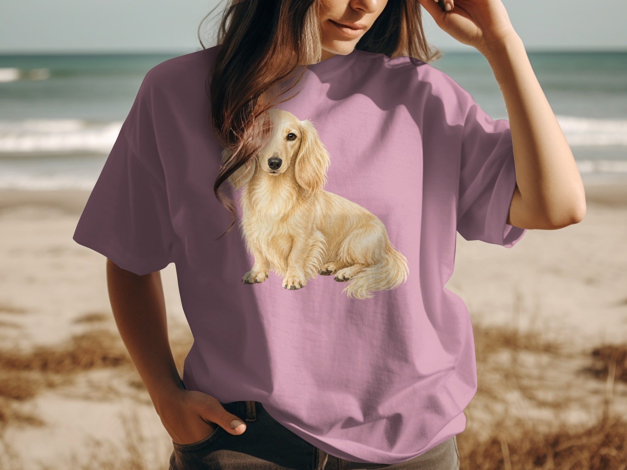 Long-haired cream dachshund printed on a mauve t-shirt at the beach.