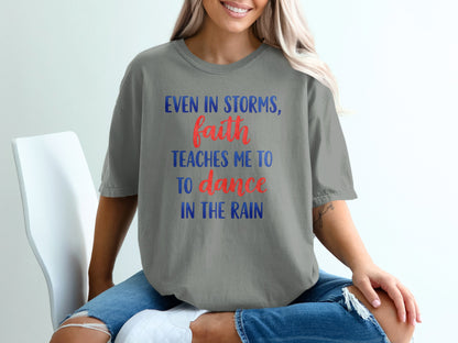 Gray t-shirt with blue and red text "Even in storms, faith teaches me to dance in the rain."