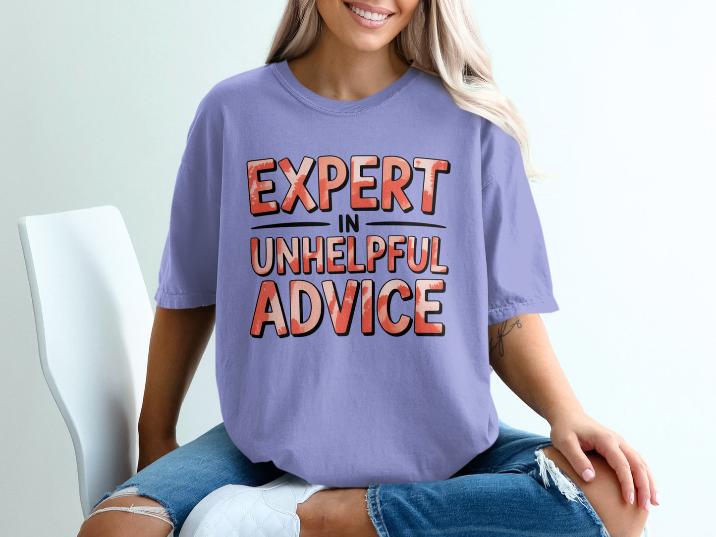 Purple t-shirt with "EXPERT IN UNHELPFUL ADVICE" text in textured orange and pink.