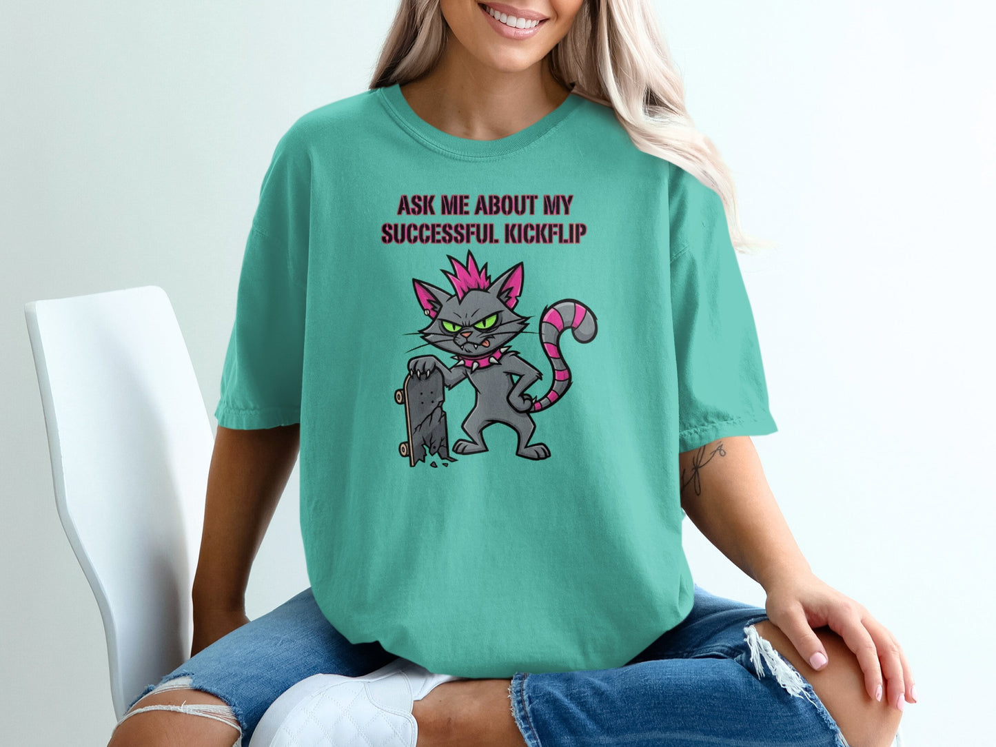 Teal t-shirt with a cartoon cat holding a skateboard and the text "Ask me about my successful kickflip."