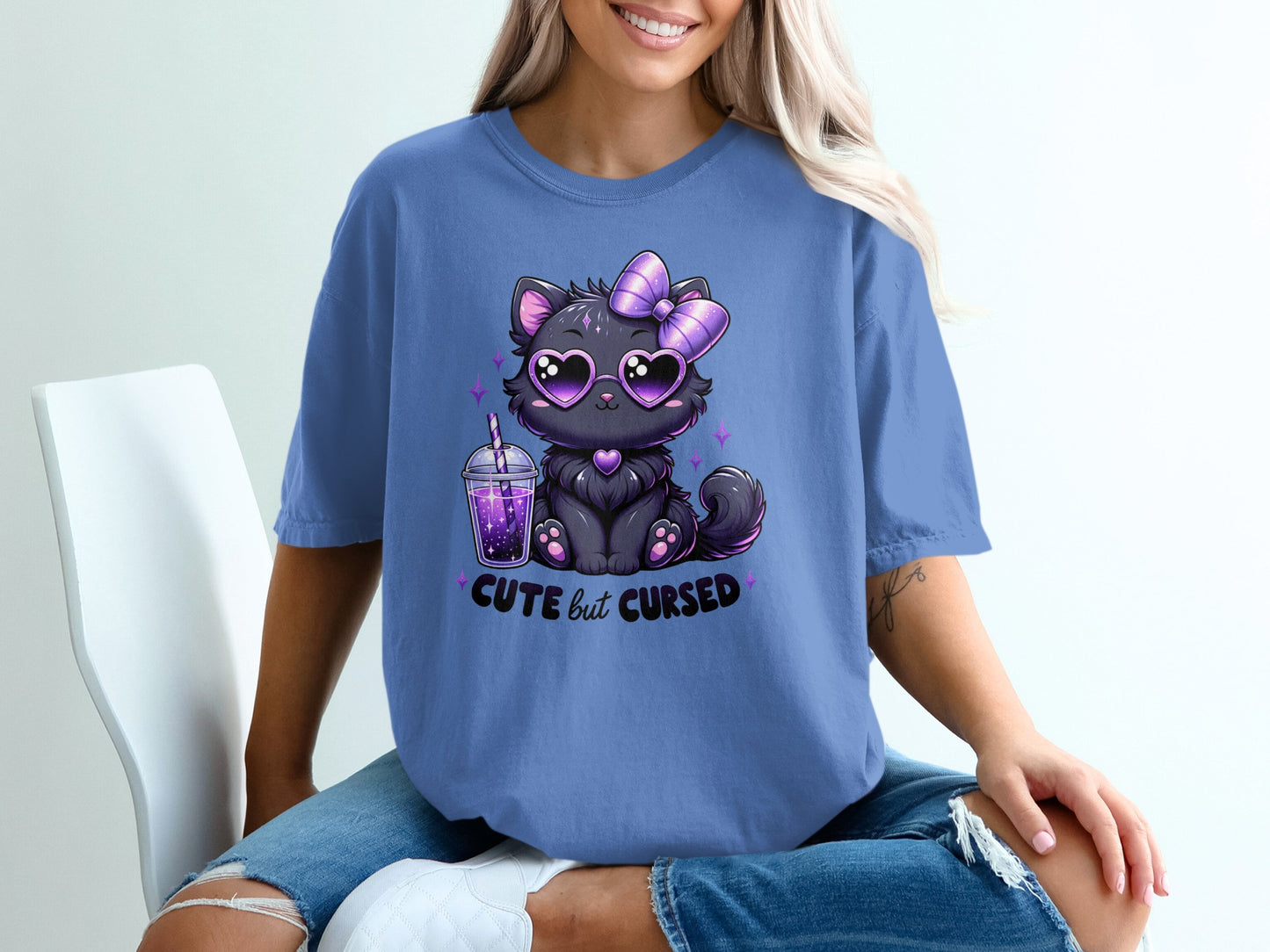 Cute black cat with heart sunglasses and bow on purple t-shirt saying "cute but cursed".