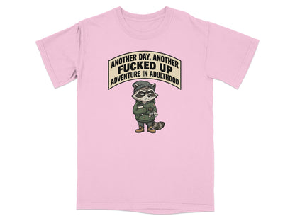 Pink t-shirt with a cartoon raccoon and text "Another day, another fucked up adventure in adulthood."
