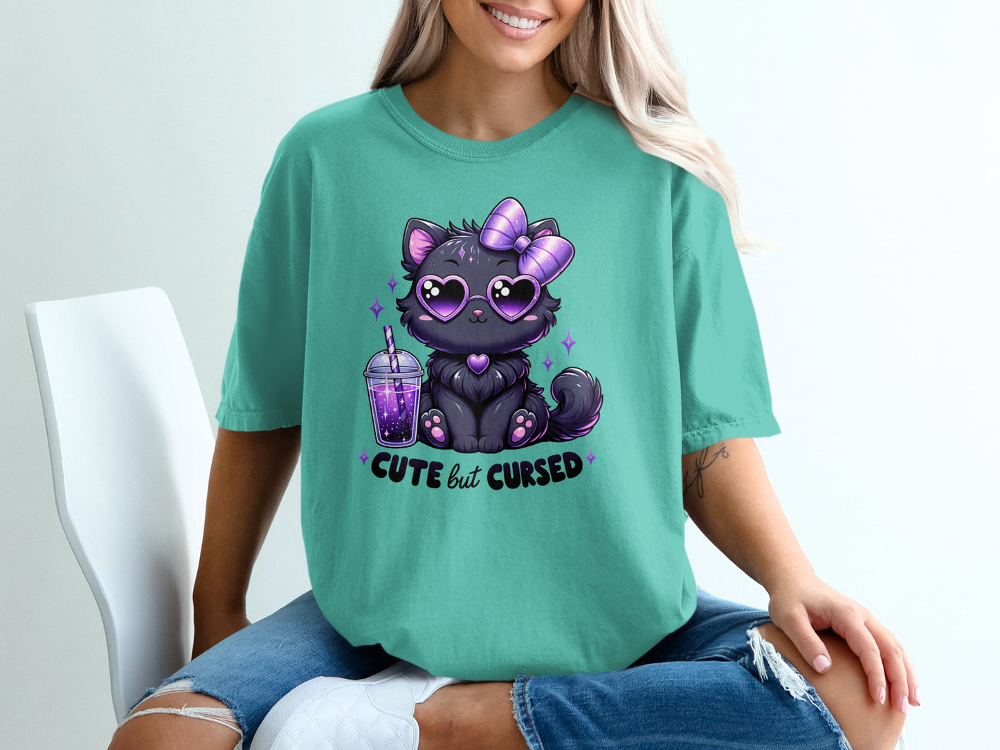 Teal t-shirt with black cat wearing heart sunglasses and bow, holding a drink.
