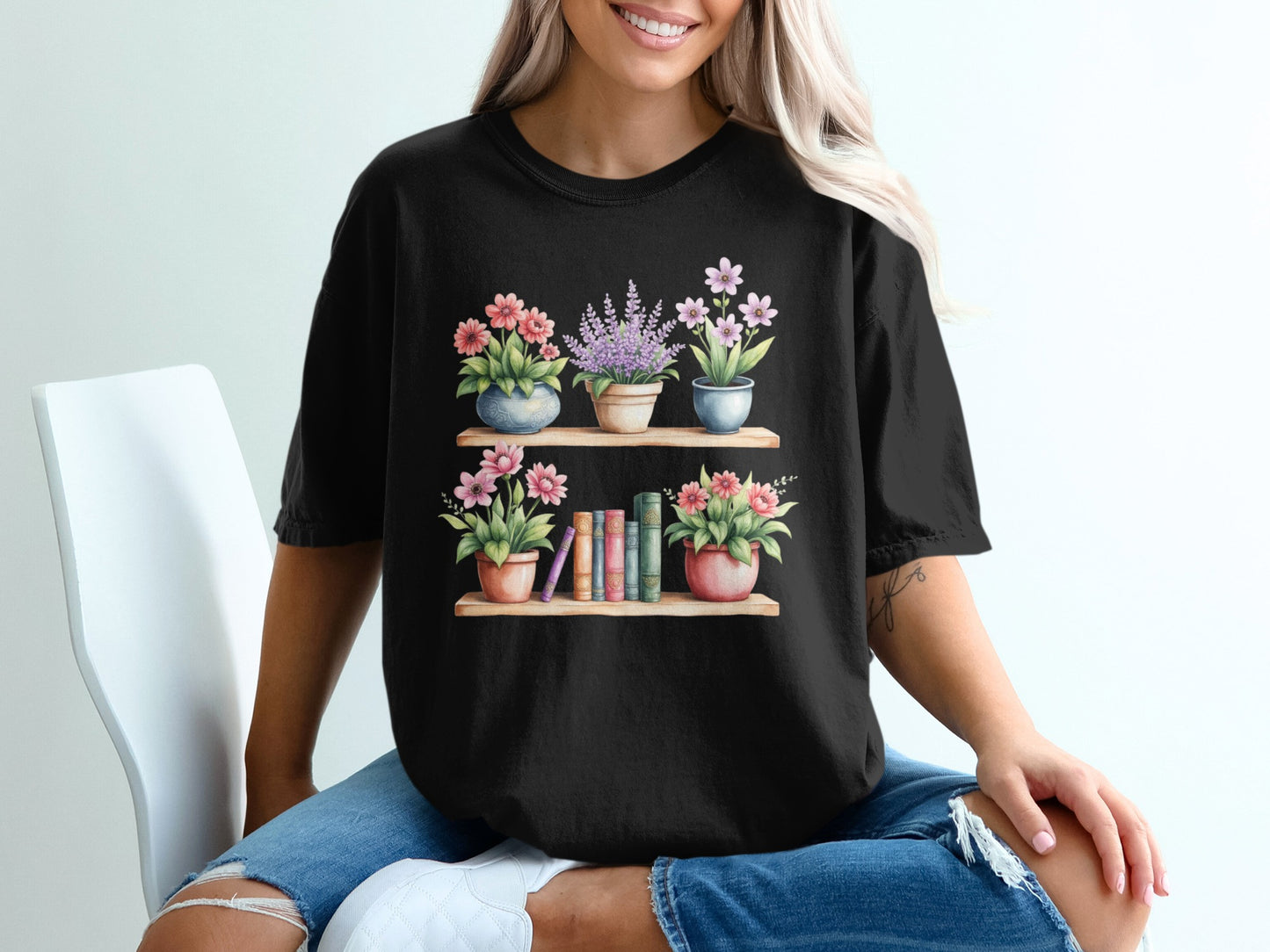 Black t-shirt with watercolor illustration of books and potted flowers on shelves.