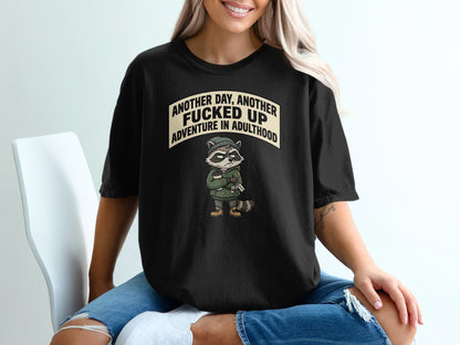 Black t-shirt with raccoon graphic and text "Another day, another f***ed up adventure in adulthood".