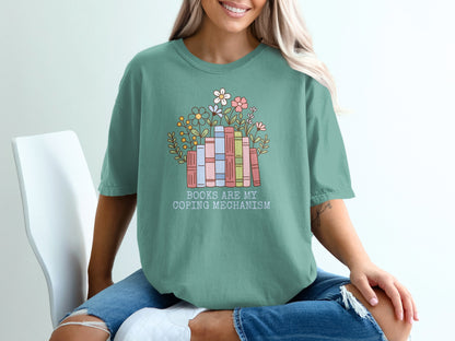 Green t-shirt with stacked books and flowers, reads "Books are my coping mechanism".