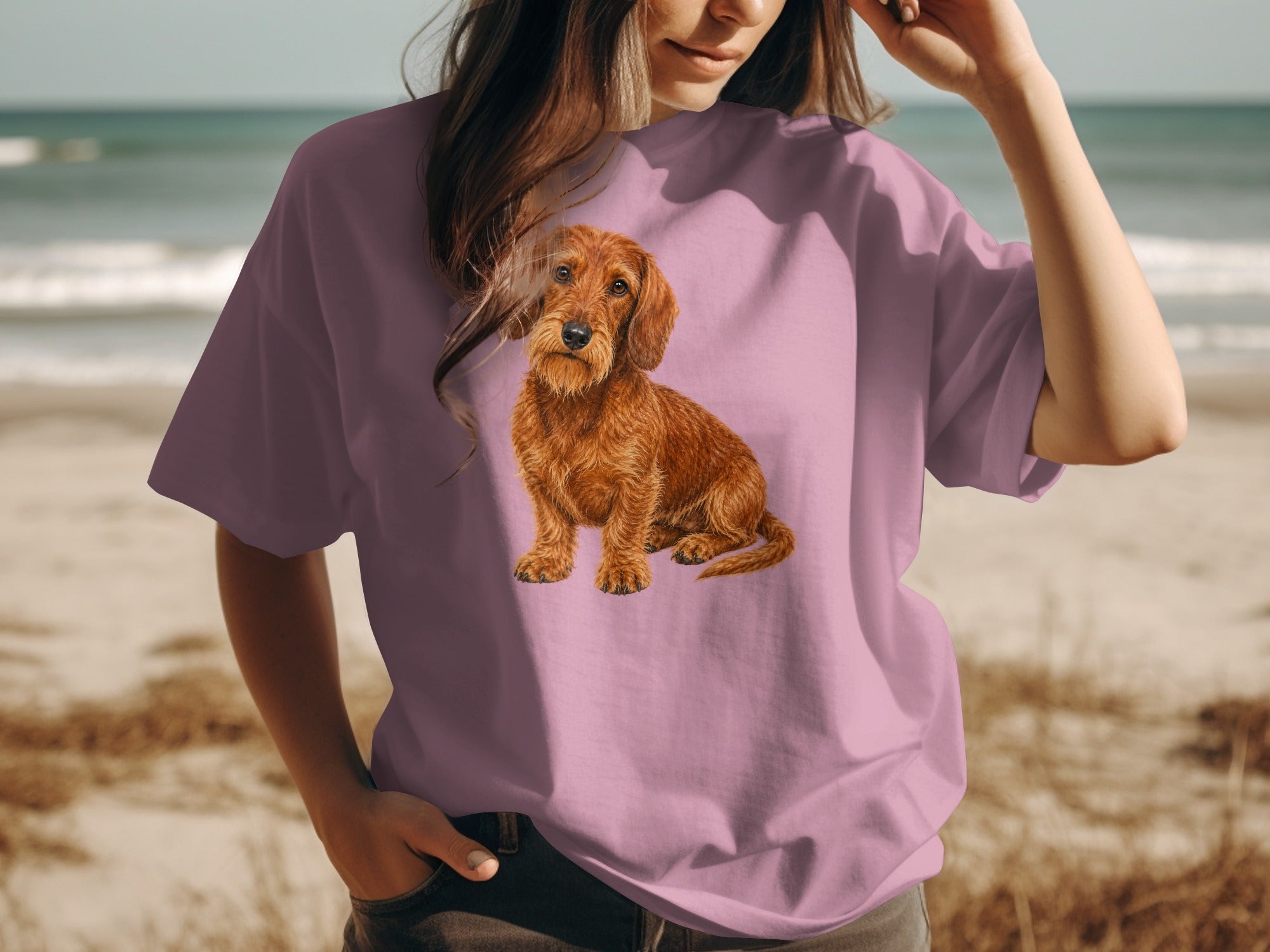 Pink t-shirt with detailed artwork of a brown wire-haired dachshund on a beach.