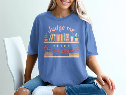 Blue t-shirt with "Judge me by my bookshelf" text and colorful bookshelf graphic.